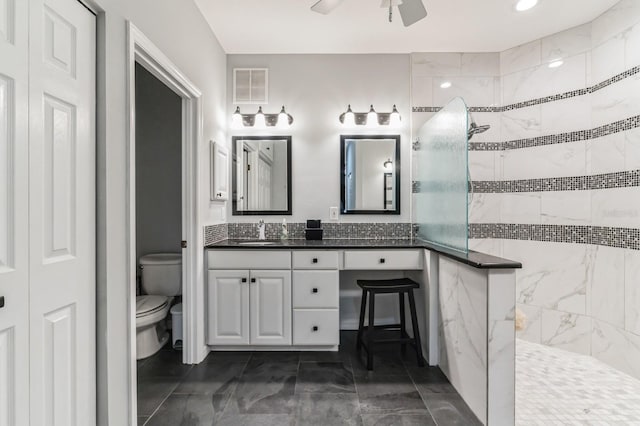 bathroom featuring ceiling fan, toilet, a tile shower, and tile patterned flooring