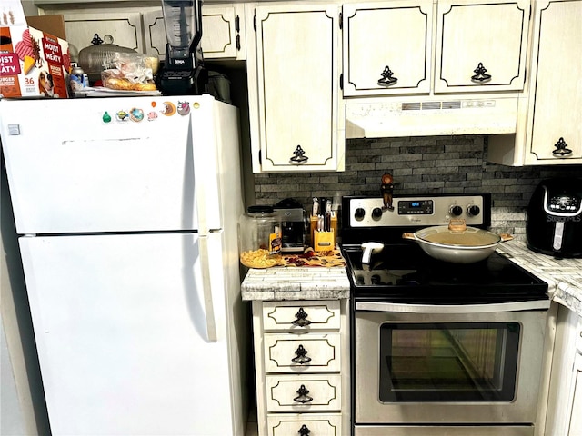 kitchen with stainless steel electric range, white fridge, cream cabinets, and decorative backsplash