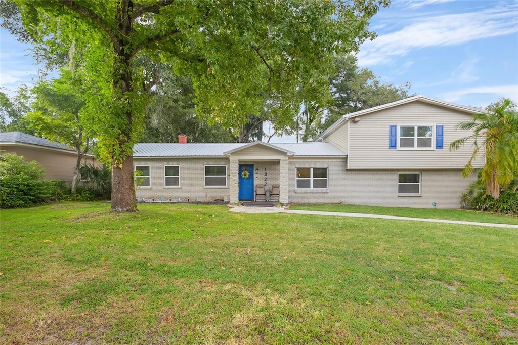 split level home featuring a front yard, brick siding, and metal roof