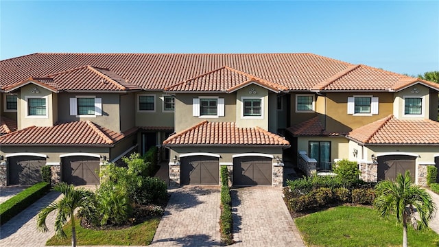 mediterranean / spanish home featuring an attached garage, stone siding, decorative driveway, and stucco siding