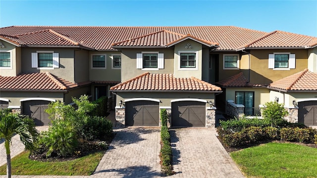 mediterranean / spanish-style home featuring decorative driveway, a tile roof, stucco siding, an attached garage, and stone siding