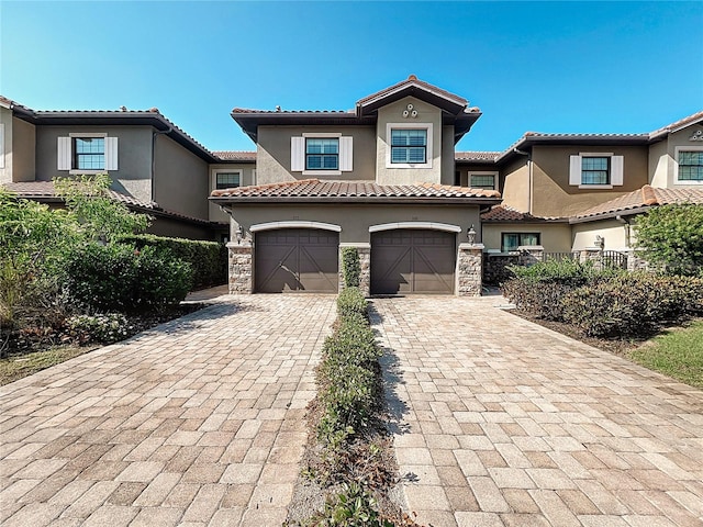 mediterranean / spanish home featuring decorative driveway, a tile roof, stucco siding, an attached garage, and stone siding