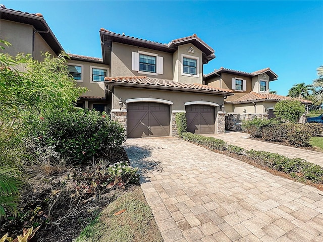 mediterranean / spanish-style house featuring a garage, stone siding, a tile roof, decorative driveway, and stucco siding