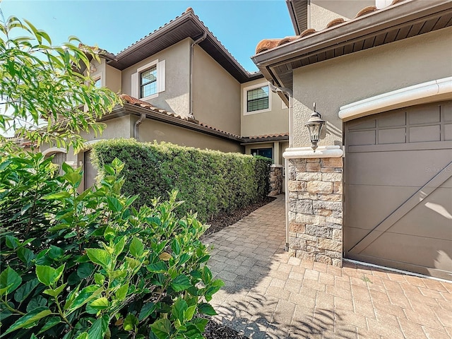 exterior space featuring a garage, stone siding, and stucco siding