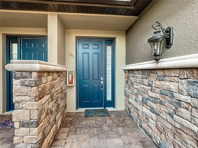 view of exterior entry featuring stone siding and stucco siding