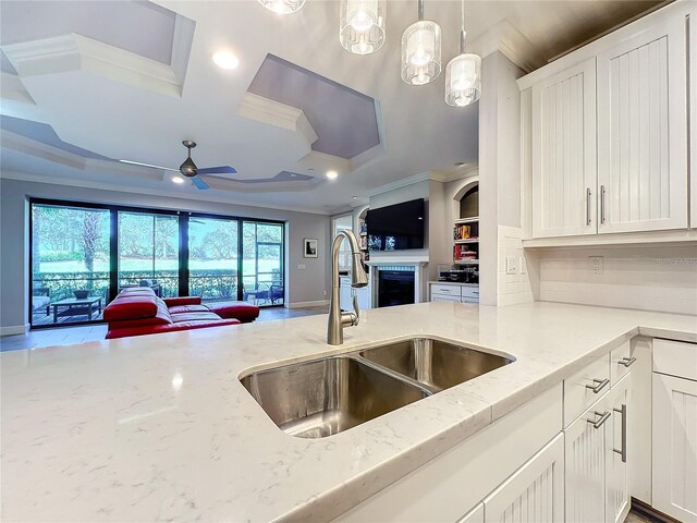 kitchen with ceiling fan with notable chandelier, sink, crown molding, and light stone counters