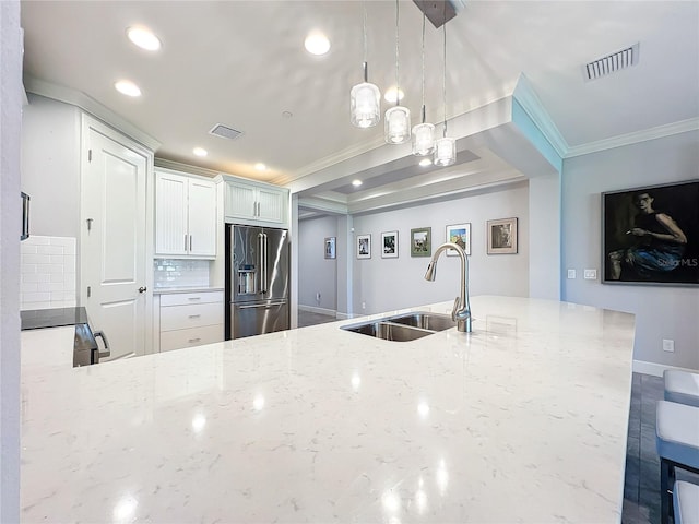 kitchen featuring backsplash, decorative light fixtures, high end refrigerator, sink, and light stone countertops