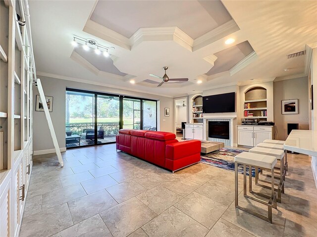 tiled living room with ceiling fan, a raised ceiling, crown molding, and built in shelves