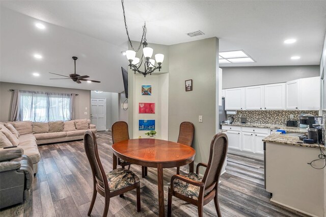 dining area featuring dark hardwood / wood-style flooring, ceiling fan with notable chandelier, and vaulted ceiling with skylight