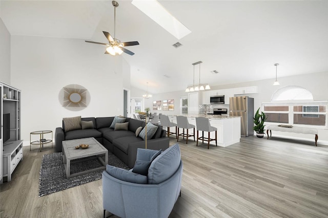 living room featuring light wood-type flooring, high vaulted ceiling, a skylight, and ceiling fan