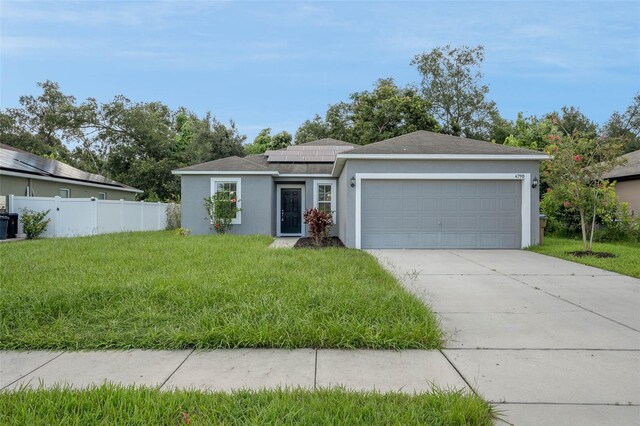 single story home featuring solar panels, an attached garage, fence, a front lawn, and stucco siding