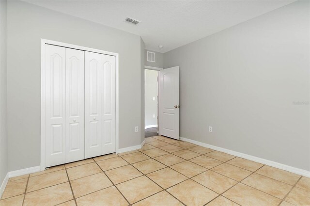 unfurnished bedroom with light tile patterned floors, baseboards, visible vents, and a closet