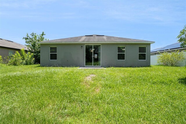 back of property with stucco siding and a yard