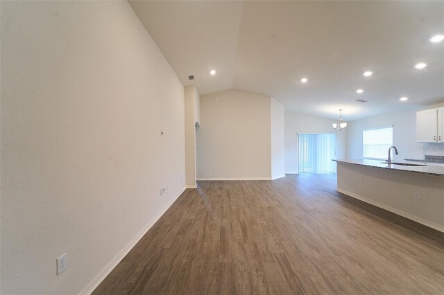 unfurnished living room with sink, vaulted ceiling, an inviting chandelier, and hardwood / wood-style floors