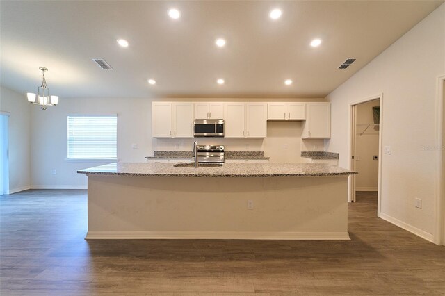 kitchen featuring appliances with stainless steel finishes, light stone counters, dark wood-type flooring, and a center island with sink