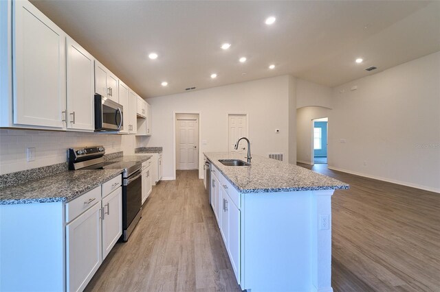 kitchen featuring light wood-type flooring, tasteful backsplash, vaulted ceiling, appliances with stainless steel finishes, and sink