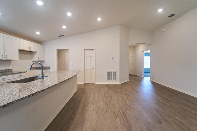 kitchen with sink, stone counters, dark hardwood / wood-style floors, vaulted ceiling, and white cabinetry