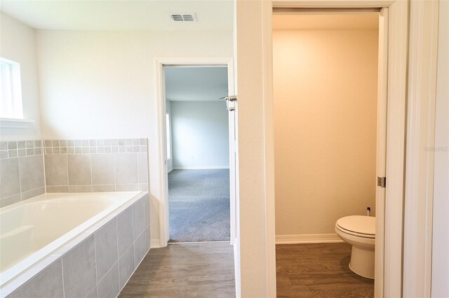 bathroom with wood-type flooring, toilet, and tiled tub