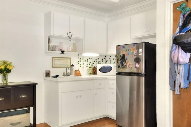 kitchen featuring white cabinetry, sink, ornamental molding, and stainless steel refrigerator