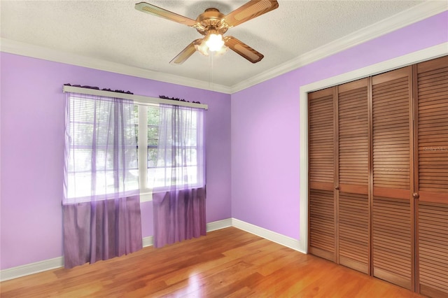 unfurnished bedroom featuring wood-type flooring, a textured ceiling, ornamental molding, a closet, and ceiling fan