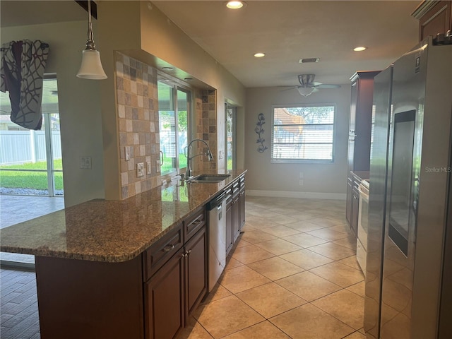 kitchen featuring dark stone counters, hanging light fixtures, stainless steel appliances, dark brown cabinets, and a sink