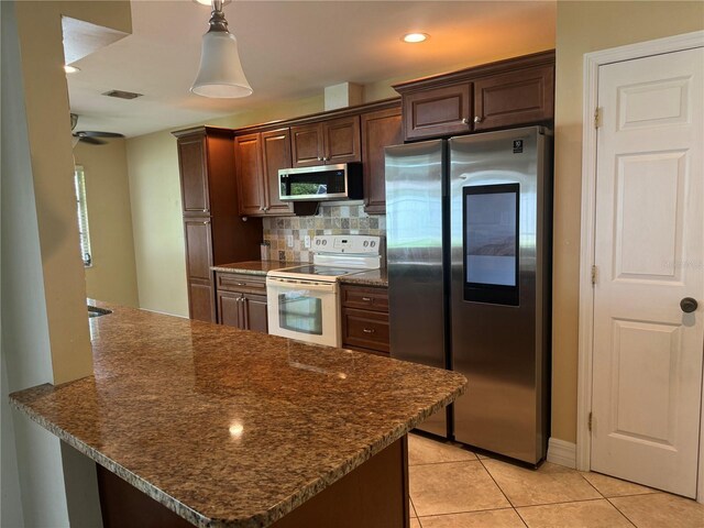 kitchen with tasteful backsplash, appliances with stainless steel finishes, light tile patterned floors, dark stone countertops, and decorative light fixtures