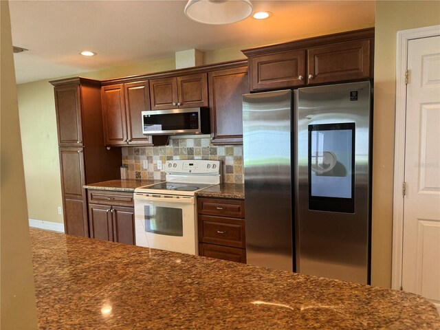 kitchen with appliances with stainless steel finishes, decorative backsplash, and dark stone countertops