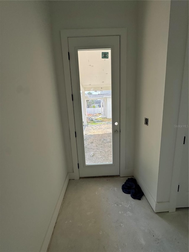 doorway to outside with unfinished concrete floors and baseboards