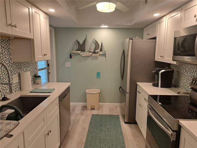 kitchen featuring light wood-type flooring, appliances with stainless steel finishes, decorative backsplash, a raised ceiling, and white cabinets