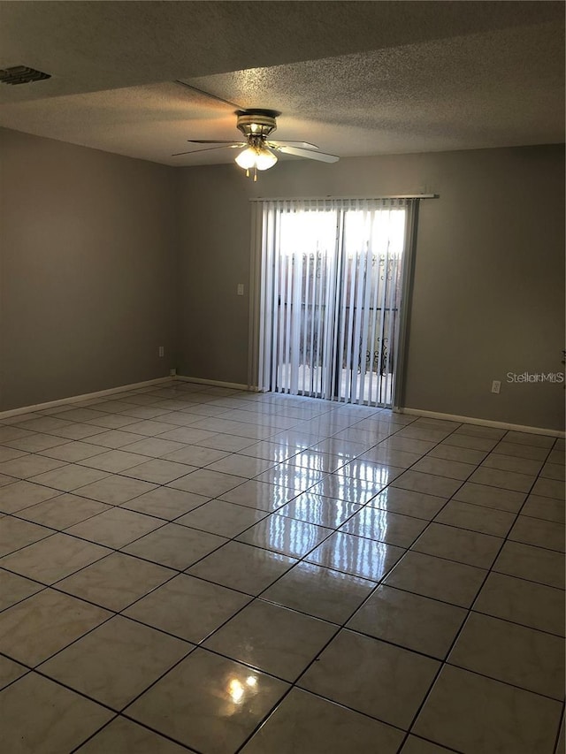 empty room with ceiling fan, a textured ceiling, and light tile patterned floors