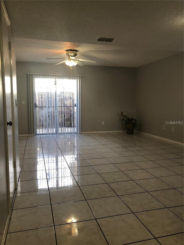 empty room featuring a textured ceiling, ceiling fan, and light tile patterned floors