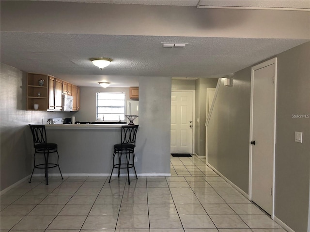 kitchen with a breakfast bar, kitchen peninsula, a textured ceiling, light tile patterned flooring, and white appliances