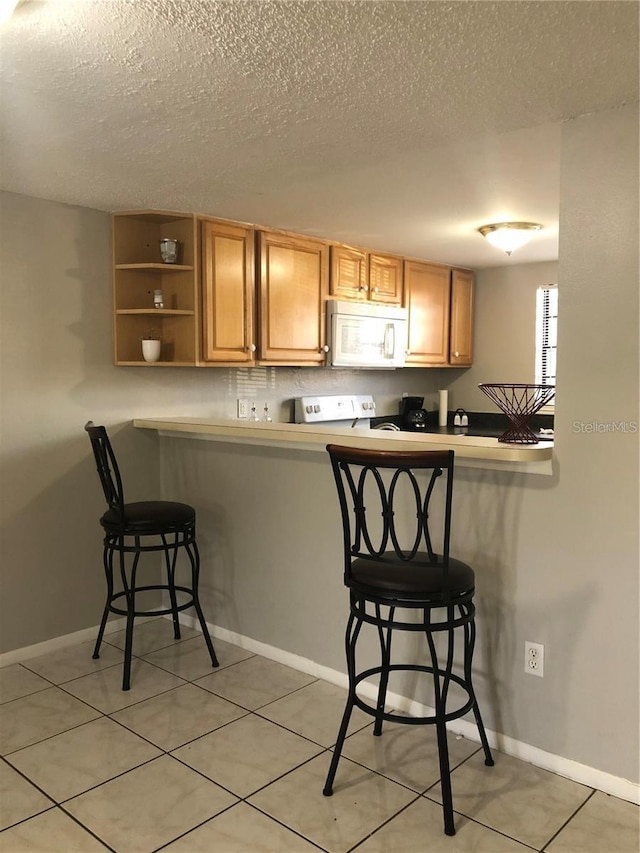 kitchen with a kitchen breakfast bar, light tile patterned floors, kitchen peninsula, a textured ceiling, and stove