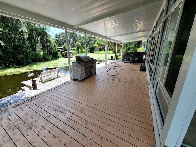 wooden terrace with a water view, a lawn, and a grill