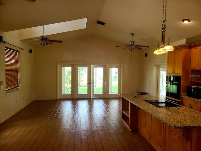 kitchen with dark wood-type flooring, ceiling fan, vaulted ceiling with skylight, and light stone countertops