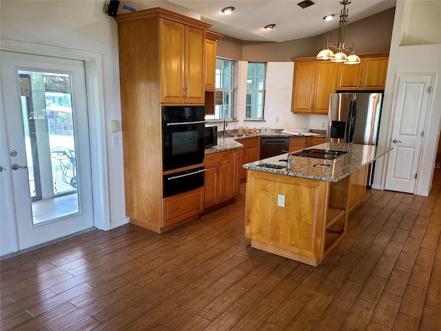 kitchen with black appliances, plenty of natural light, a center island, and light stone countertops