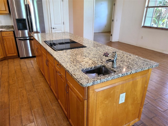 kitchen featuring a center island with sink, hardwood / wood-style floors, stainless steel fridge with ice dispenser, black electric cooktop, and light stone counters