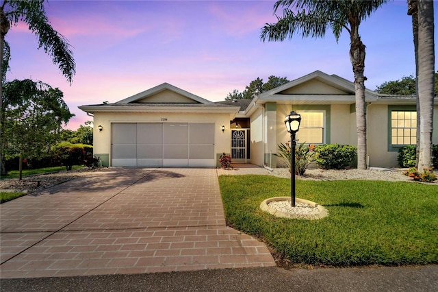 single story home featuring a garage, decorative driveway, a lawn, and stucco siding