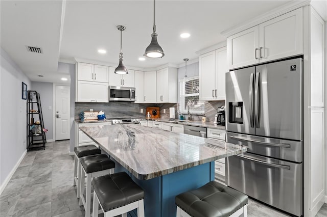 kitchen featuring appliances with stainless steel finishes, decorative light fixtures, decorative backsplash, light stone countertops, and a center island