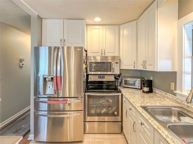 kitchen featuring stainless steel appliances, white cabinetry, sink, light stone counters, and light tile patterned floors