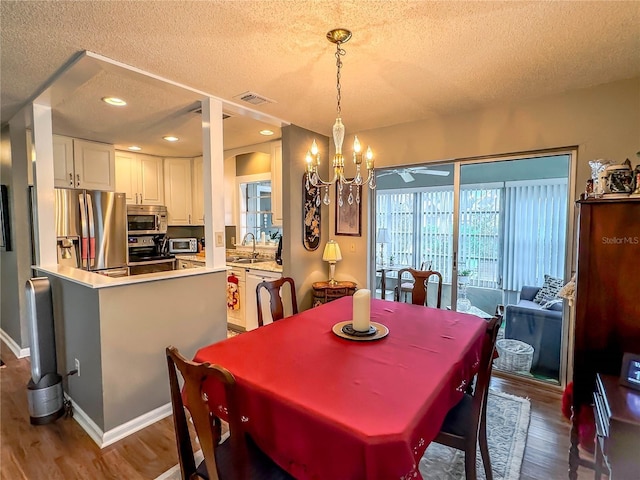 dining space with an inviting chandelier, hardwood / wood-style flooring, sink, and a textured ceiling