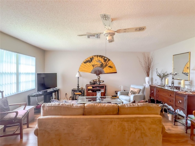 living room featuring ceiling fan, light hardwood / wood-style flooring, and a textured ceiling