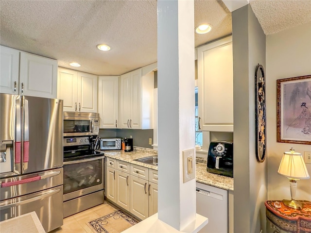 kitchen featuring white cabinets, light stone countertops, a textured ceiling, light tile patterned flooring, and stainless steel appliances