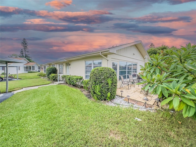 property exterior at dusk featuring a patio area and a lawn