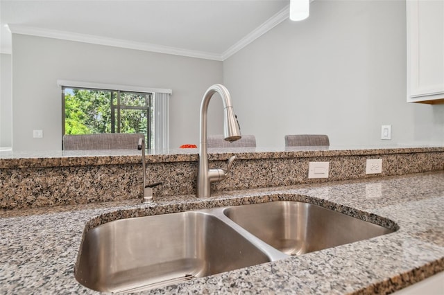 room details with light stone countertops, ornamental molding, white cabinets, and a sink