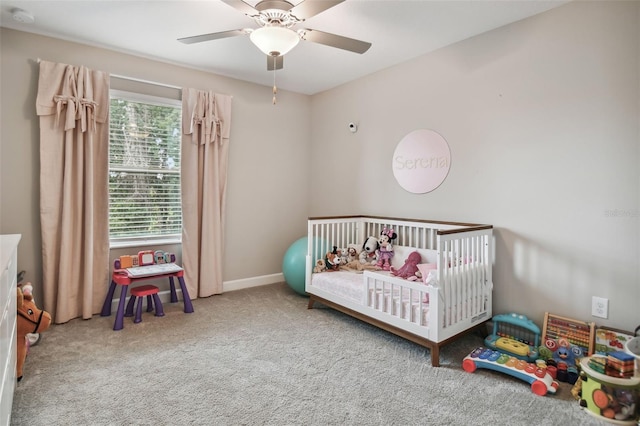 carpeted bedroom featuring a ceiling fan, a crib, and baseboards