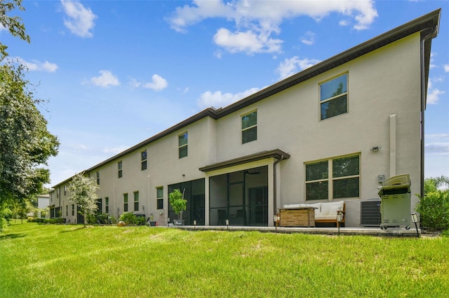 rear view of house with a sunroom, a lawn, and stucco siding