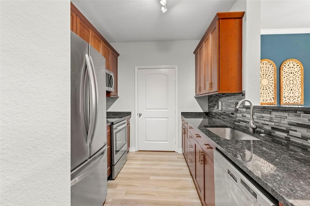 kitchen with backsplash, sink, dark stone countertops, appliances with stainless steel finishes, and light hardwood / wood-style floors