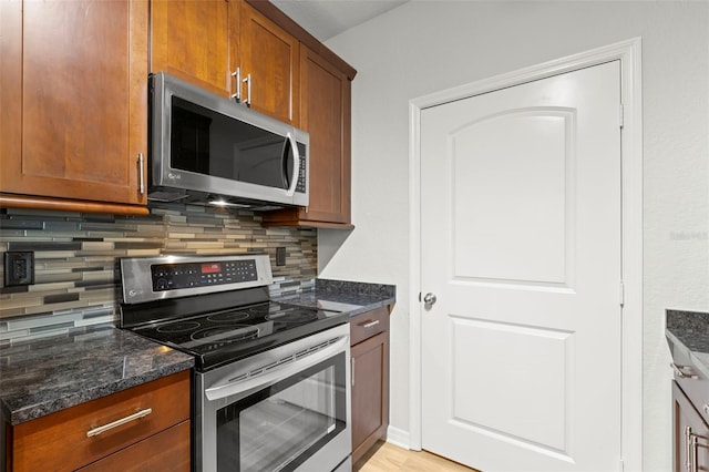 kitchen with light wood-type flooring, appliances with stainless steel finishes, dark stone countertops, and backsplash