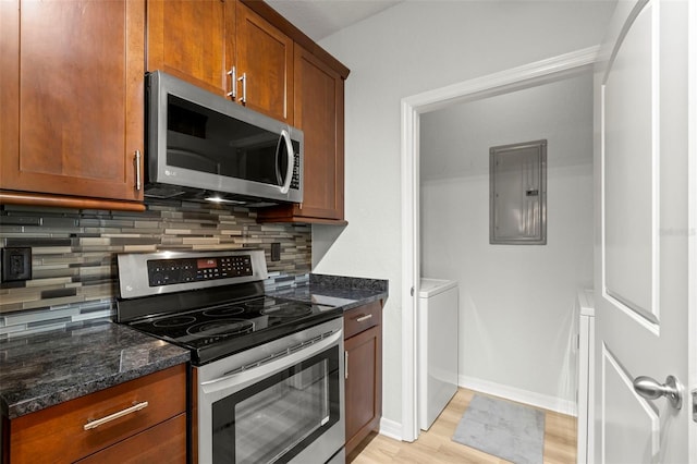 kitchen with light wood-type flooring, stainless steel appliances, dark stone countertops, and electric panel